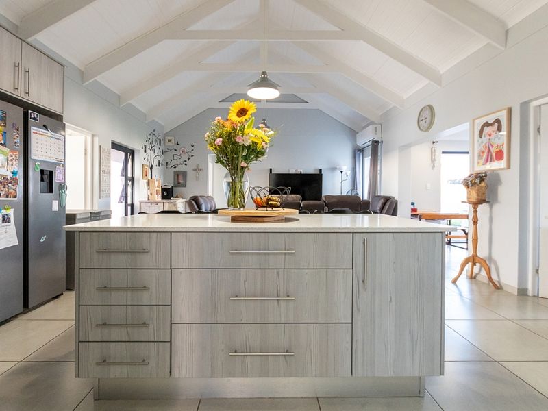 Spacious open-plan living area featuring a modern kitchen island, vaulted ceilings with exposed beams, and neutral tiled flooring throughout.