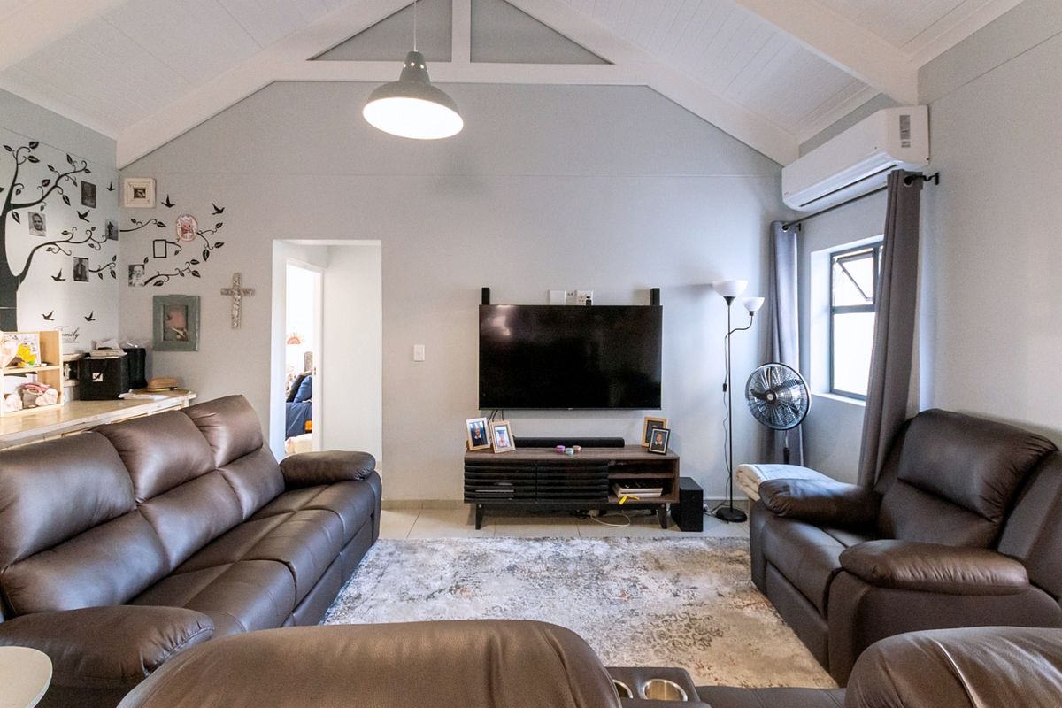 A comfortable living room featuring a high vaulted ceiling, tiled flooring, and a wall-mounted split-system air conditioner for climate control.