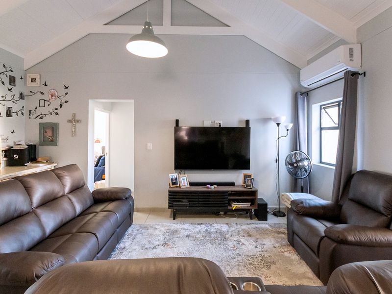 A comfortable living room featuring a high vaulted ceiling, tiled flooring, and a wall-mounted split-system air conditioner for climate control.
