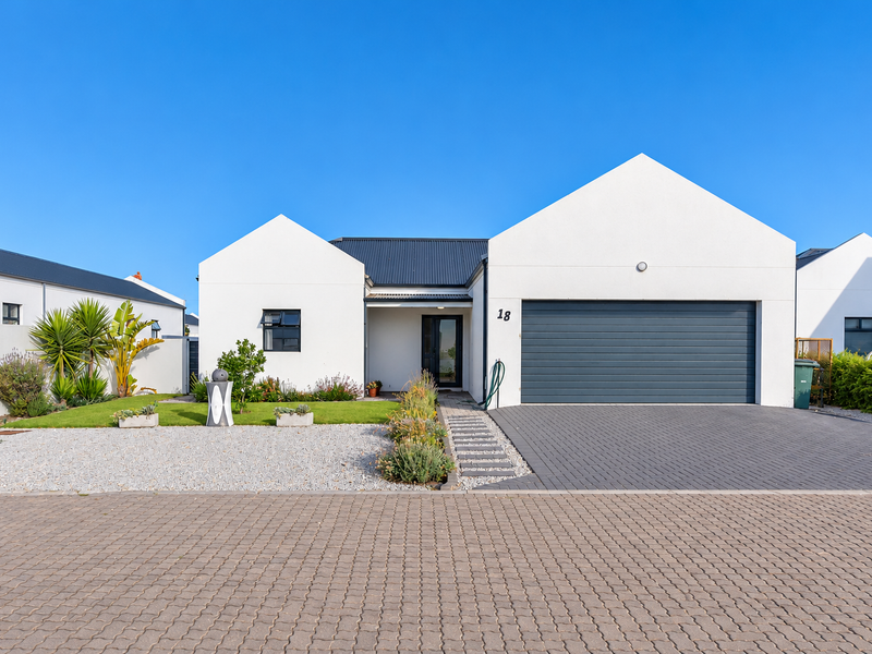 Modern single-story residence featuring a clean white facade, dark metal roof, double garage, and a neatly landscaped front garden with paved driveway.
