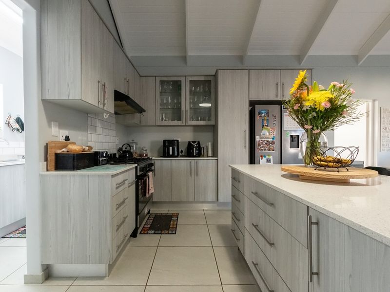 Modern kitchen featuring light wood-grain cabinetry, a spacious central island with stone countertops, subway tile backsplash, and exposed beam ceilings.