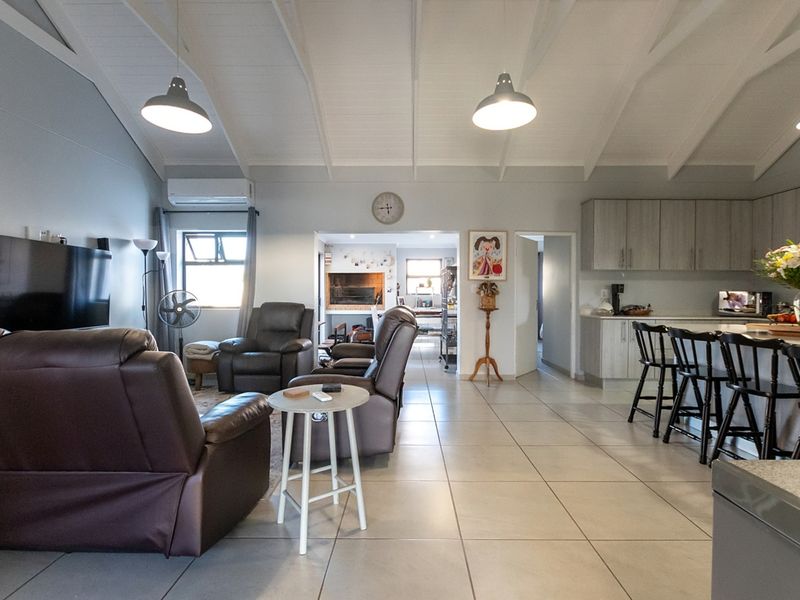 Spacious open-plan living area featuring a vaulted ceiling, tiled floors, modern kitchen cabinetry, and a central island, seamlessly connecting to a cozy fireplace area.