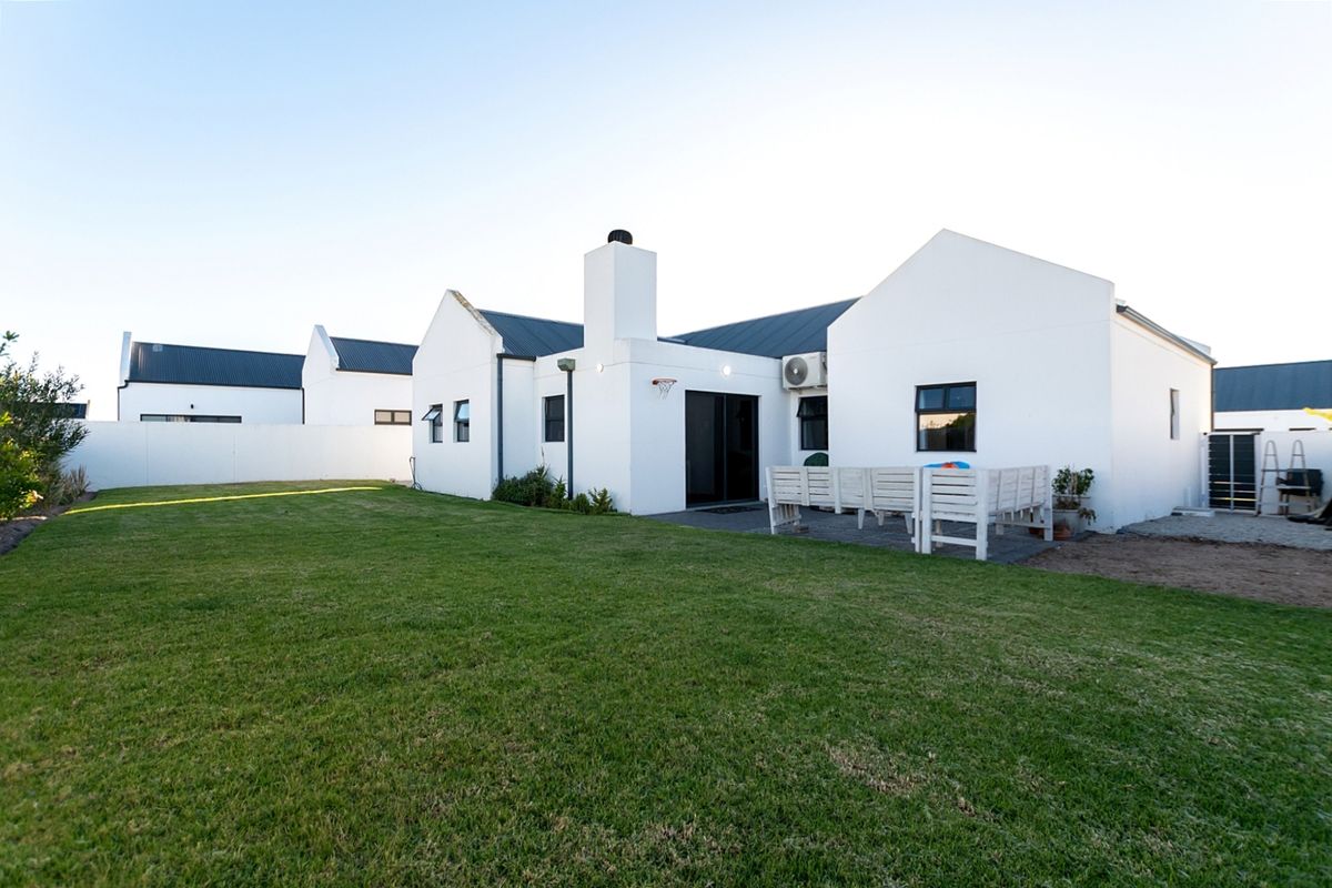Rear view of a modern white house featuring a corrugated metal roof, chimney, paved patio area, and a well-maintained lawn.