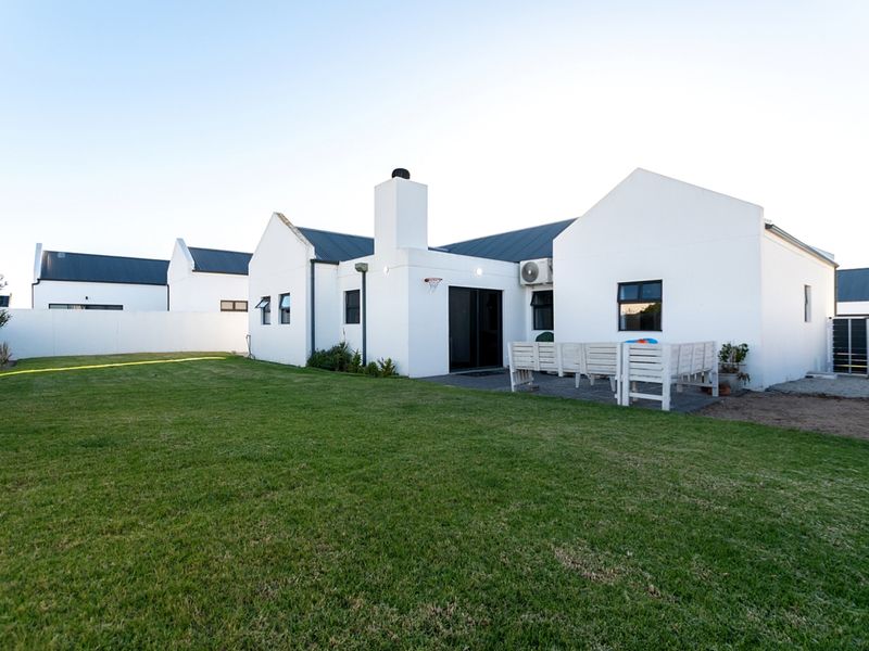 Rear view of a modern white house featuring a corrugated metal roof, chimney, paved patio area, and a well-maintained lawn.