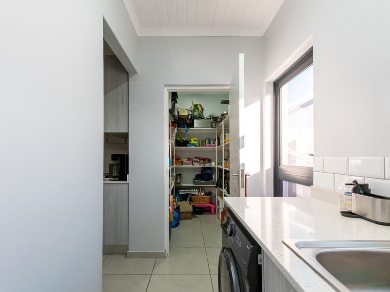 A functional scullery featuring stone countertops, an undermount sink, subway tile backsplash, and a dedicated walk-in pantry with ample shelving.