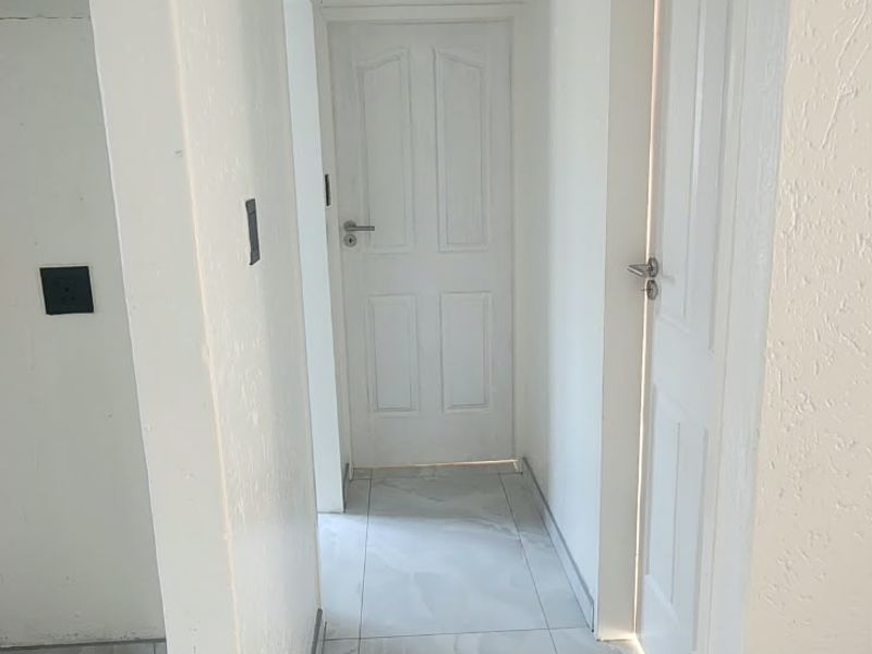 A clean, bright hallway featuring modern light-toned floor tiles and white internal doors, providing a neutral transition between living spaces.