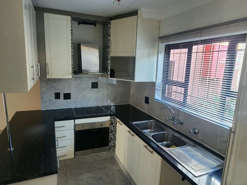 A functional kitchen featuring built-in cabinetry, black granite countertops, a stainless steel double sink, and integrated oven and hob with an extractor fan.