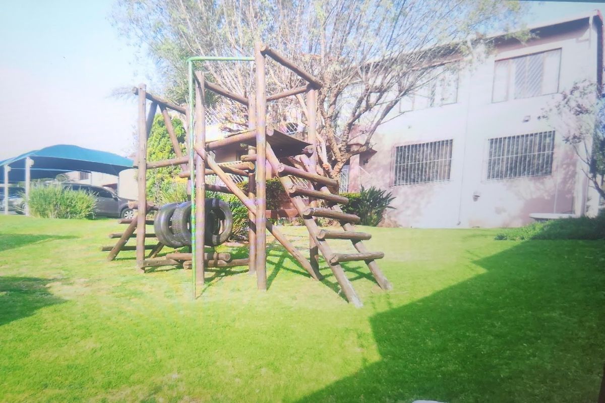 A rear garden area featuring a wooden jungle gym, lawn, and a view of the building exterior with security bars on the windows.