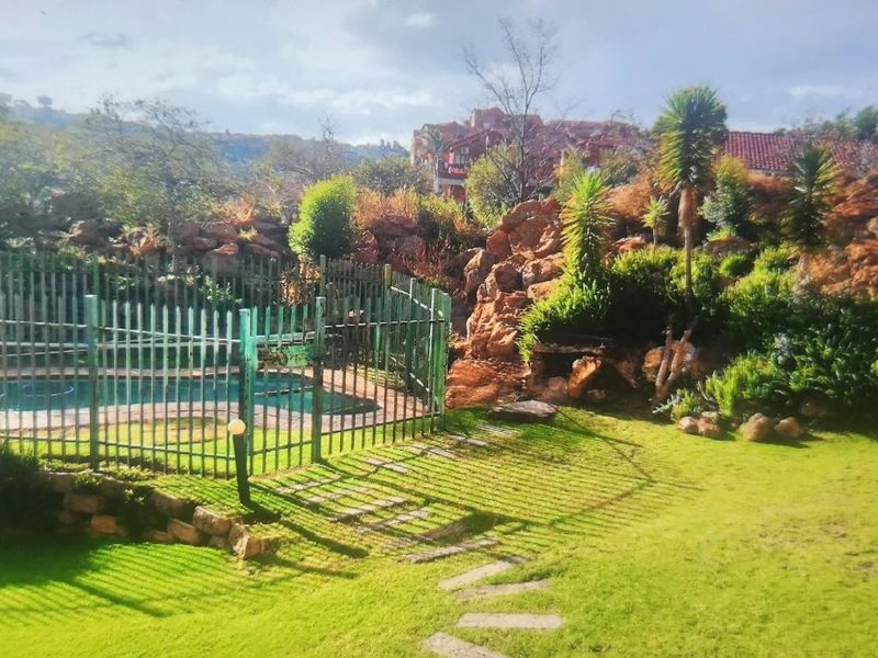 A landscaped garden area featuring a fenced swimming pool, natural stone retaining walls, and a stone pathway set against a scenic backdrop.