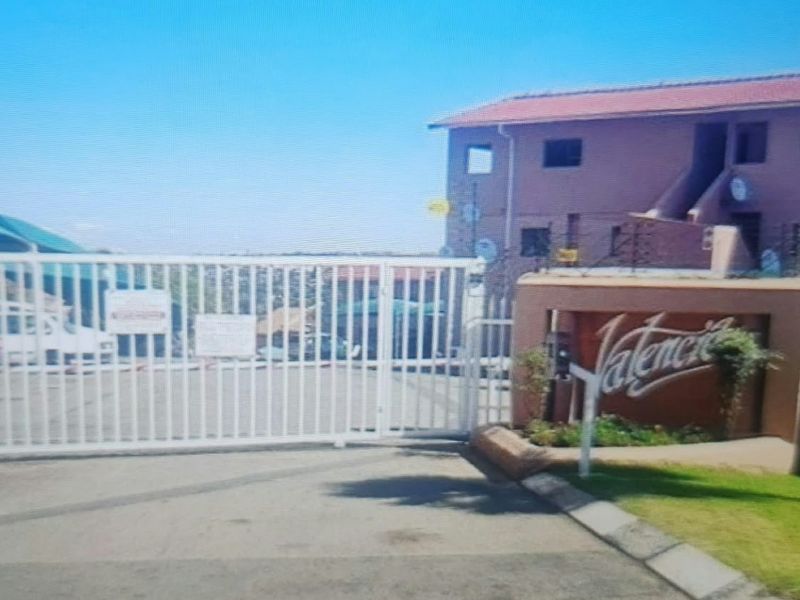 Front entrance view of the Valencia apartment complex featuring a secure sliding gate, intercom system, and perimeter electric fencing.