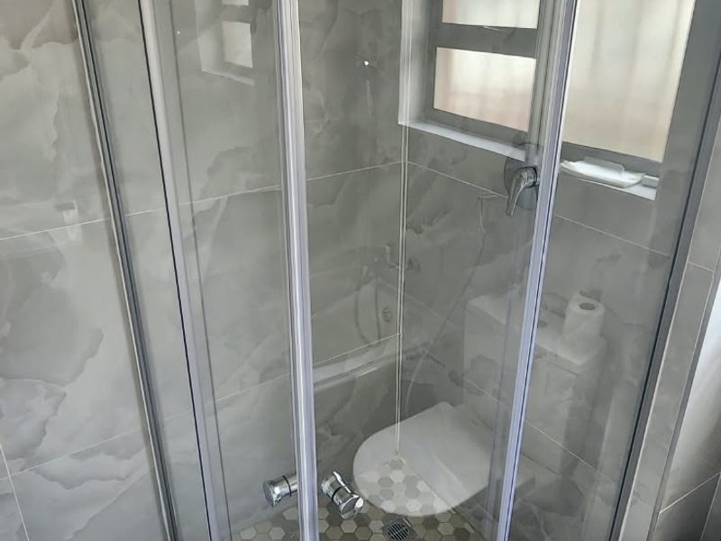 A modern bathroom featuring a glass-enclosed shower with grey marble-effect wall tiles and contrasting hexagonal floor tiles.