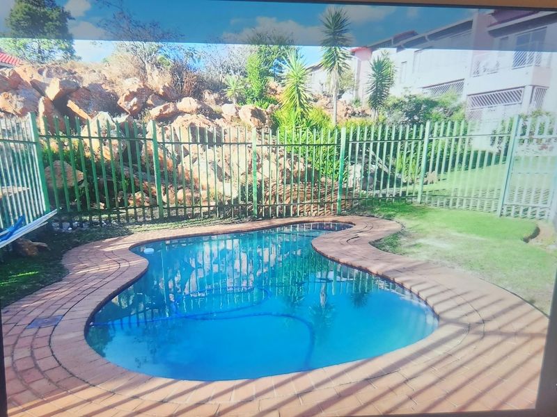 A private swimming pool area featuring brick coping, surrounded by a metal fence and a natural rock garden backdrop.