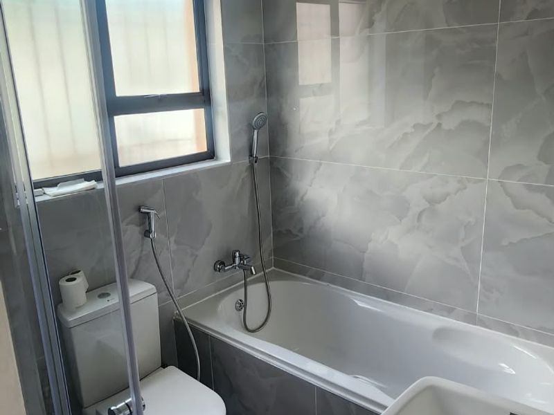 A modern, tiled bathroom featuring a bathtub, wall-mounted basin, and toilet, finished with contemporary grey marble-look tiles.