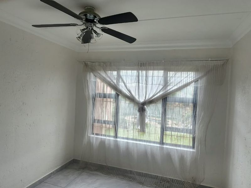 A bright, empty bedroom featuring tiled flooring, a ceiling fan, and security bars on the window.