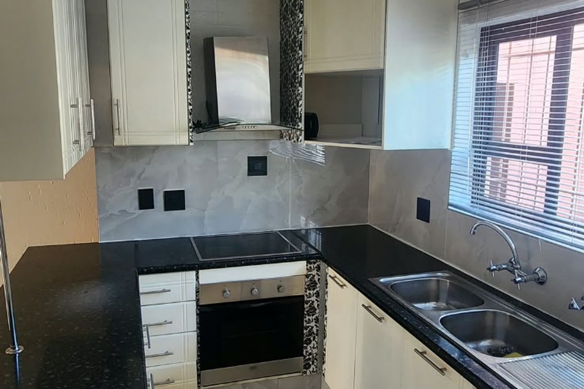 A functional kitchen featuring cream cabinetry, dark granite countertops, built-in oven and hob, and tiled flooring with a neutral backsplash.