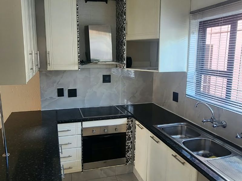 A functional kitchen featuring cream cabinetry, dark granite countertops, built-in oven and hob, and tiled flooring with a neutral backsplash.