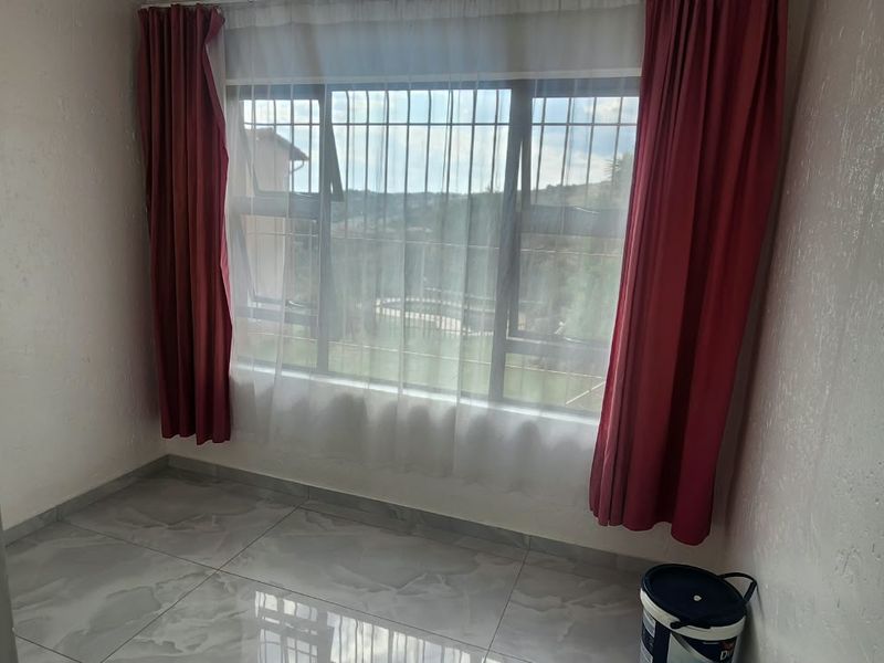A bright, empty bedroom featuring modern tiled flooring and large windows fitted with security bars, offering a clean canvas for personalization.