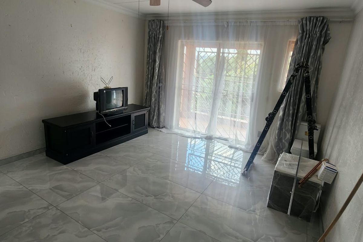 A living room featuring large format porcelain floor tiles, a sliding glass door with security gate, and a ceiling fan.