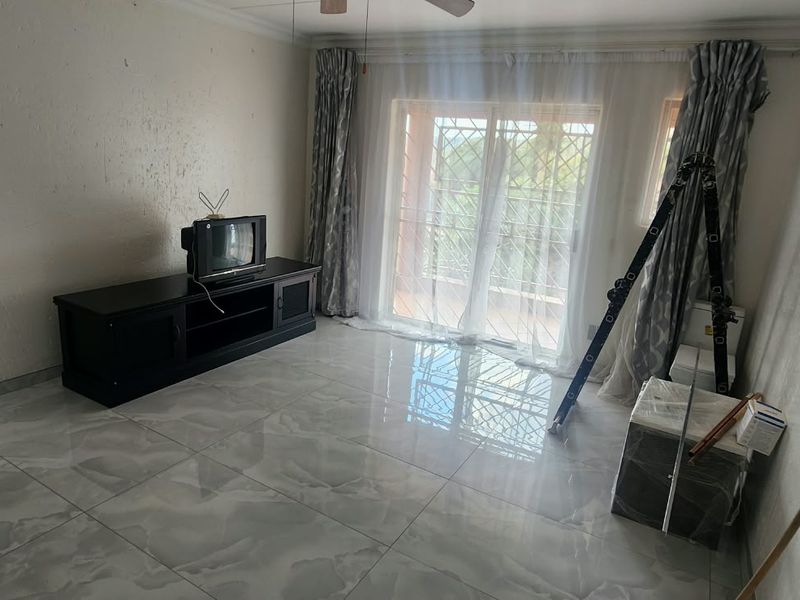 A living room featuring large format porcelain floor tiles, a sliding glass door with security gate, and a ceiling fan.