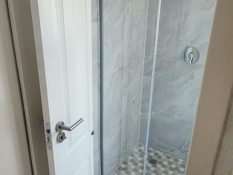 A modern bathroom featuring a glass-enclosed shower with marble-effect wall tiles and decorative hexagonal floor tiling.