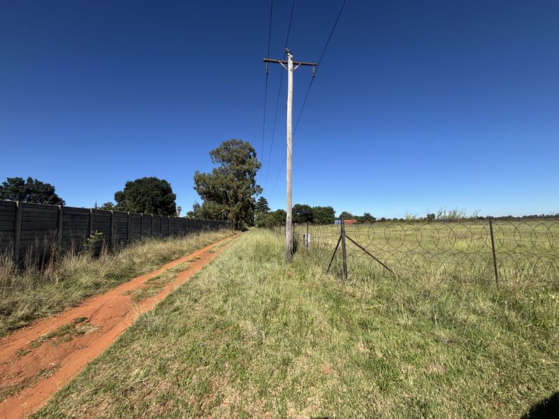 A view of the vacant residential land featuring a dirt access path, precast concrete boundary wall, and perimeter fencing with razor wire.