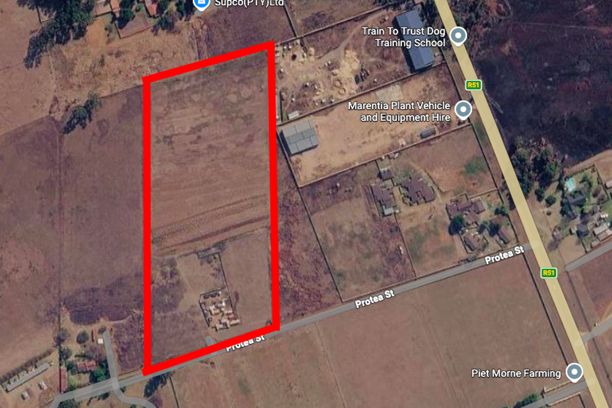 Aerial view of a large, rectangular vacant residential plot with clear boundary markings, situated near local infrastructure and road access.