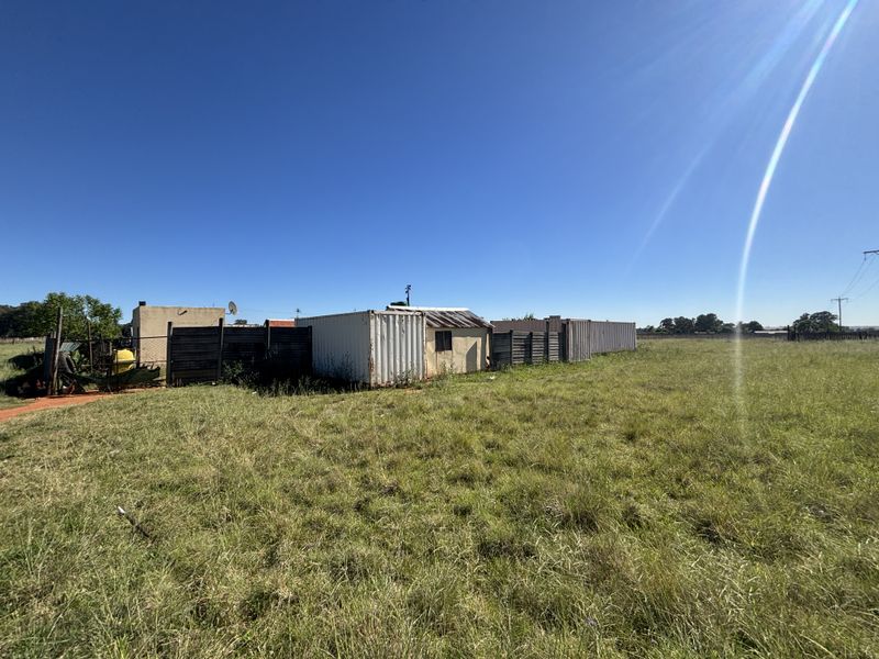 A vacant residential plot featuring a shipping container structure and perimeter timber fencing, set within an open grassy landscape.