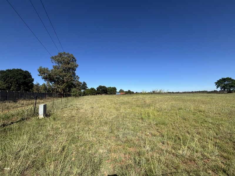A wide-angle view of a vacant residential plot featuring open grass, perimeter fencing, and existing utility connections.