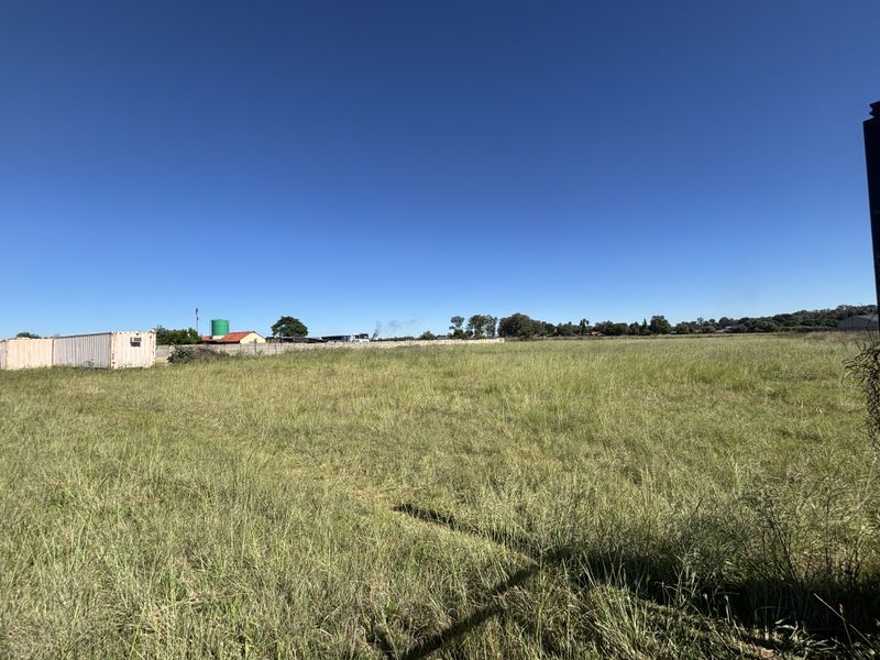 A wide-angle view of a vacant residential plot featuring open grassland and perimeter fencing under a clear blue sky.