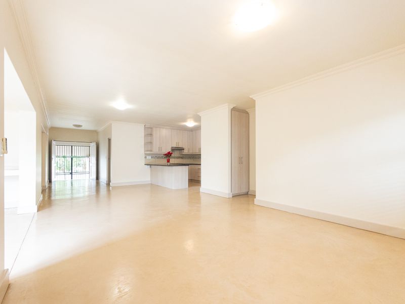 Spacious open-plan living area featuring polished concrete floors, coved cornicing, and a functional kitchen with built-in cabinetry and an extractor fan.