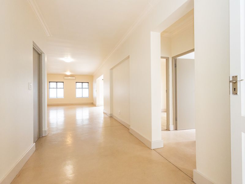 A bright and spacious hallway featuring polished concrete floors, coved cornicing, and neutral walls, leading into an open-plan living area with air conditioning.