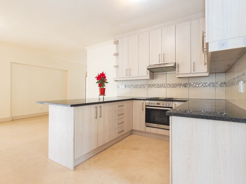 Modern open-plan kitchen featuring light wood-finish cabinetry, granite countertops, and integrated appliances, seamlessly flowing into the adjacent living area.