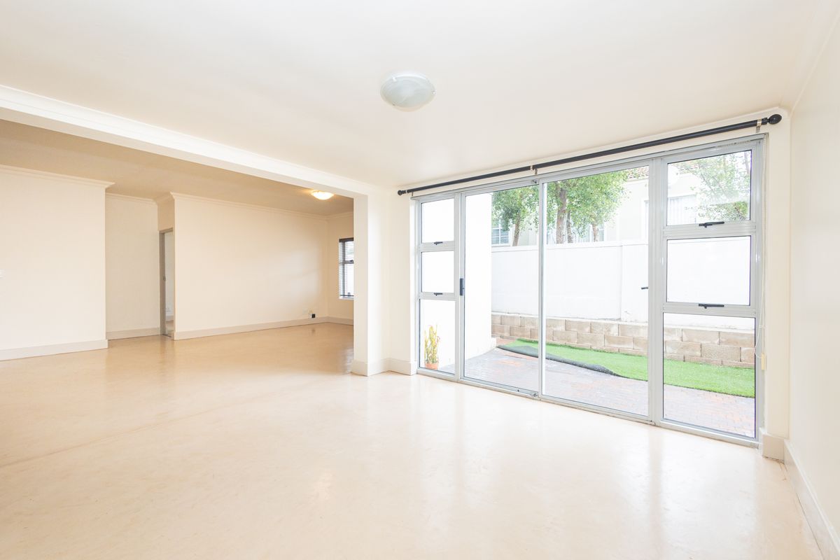 Spacious, light-filled living area featuring neutral flooring, cove cornicing, and large sliding glass doors providing direct access to the outdoor patio area.
