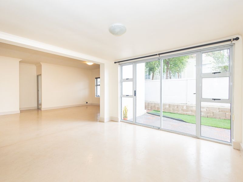 Spacious, light-filled living area featuring neutral flooring, cove cornicing, and large sliding glass doors providing direct access to the outdoor patio area.