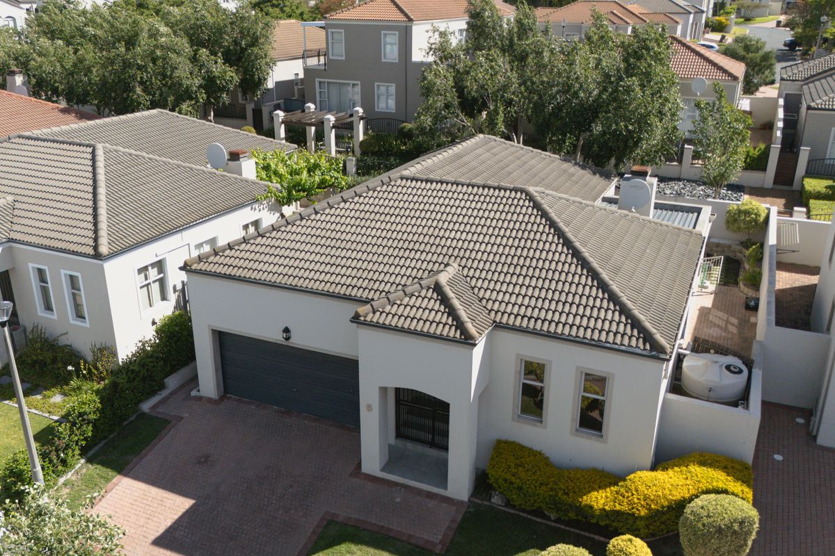 Aerial view of a residential property featuring a tiled roof, paved driveway, and a double garage within a secure estate setting.