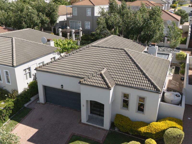Aerial view of a residential property featuring a tiled roof, paved driveway, and a double garage within a secure estate setting.