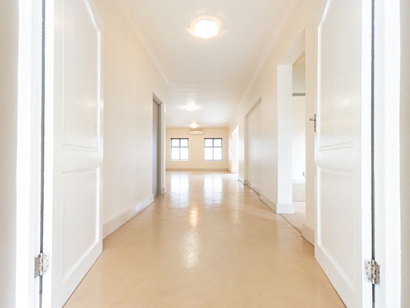 A bright and spacious hallway featuring neutral finishes, clean lines, and polished flooring, leading into an open-plan living area with an integrated air conditioning unit.