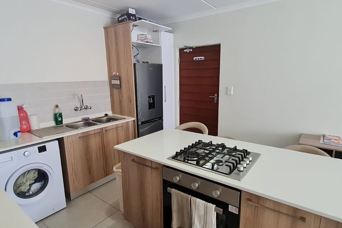 Modern kitchen featuring wood-finish cabinetry, a central island with a gas hob and oven, and integrated laundry facilities.