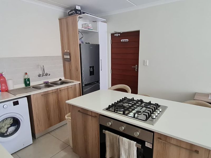 Modern kitchen featuring wood-finish cabinetry, a central island with a gas hob and oven, and integrated laundry facilities.