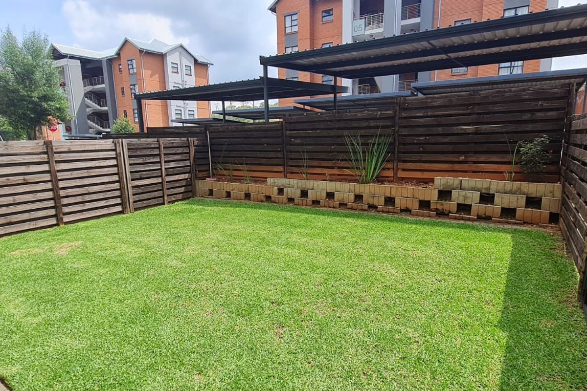 A private rear garden featuring a well-maintained lawn, paved patio area, and timber slat perimeter fencing with a low concrete block retaining wall.