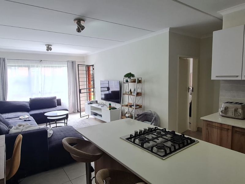 Open-plan living area featuring a modern kitchen with stone countertops, gas hob, and tiled flooring, seamlessly flowing into a comfortable lounge space.