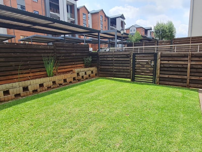 A private rear garden featuring a well-maintained lawn, timber slat fencing, a brick retaining wall, and a paved walkway leading to the townhouse entrance.
