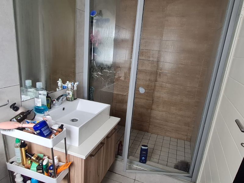 A functional bathroom featuring a modern vessel sink vanity, a tiled shower enclosure with a sliding door, and neutral wall tiling.