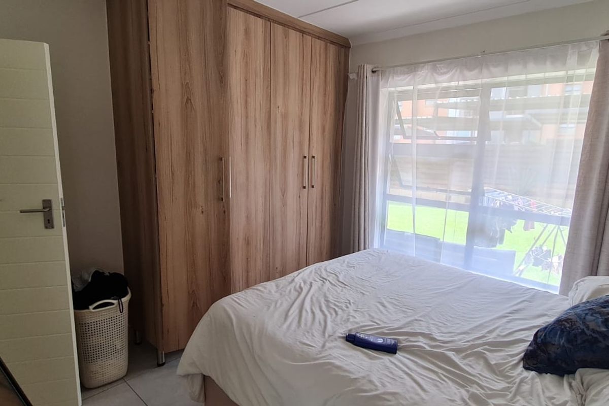 A well-lit bedroom featuring built-in wooden cupboards, tiled flooring, and a large window providing natural light.