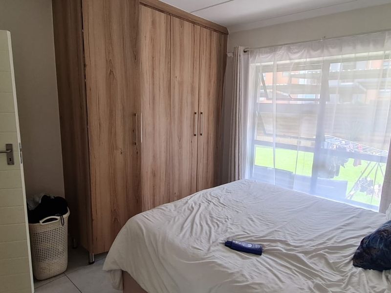 A well-lit bedroom featuring built-in wooden cupboards, tiled flooring, and a large window providing natural light.