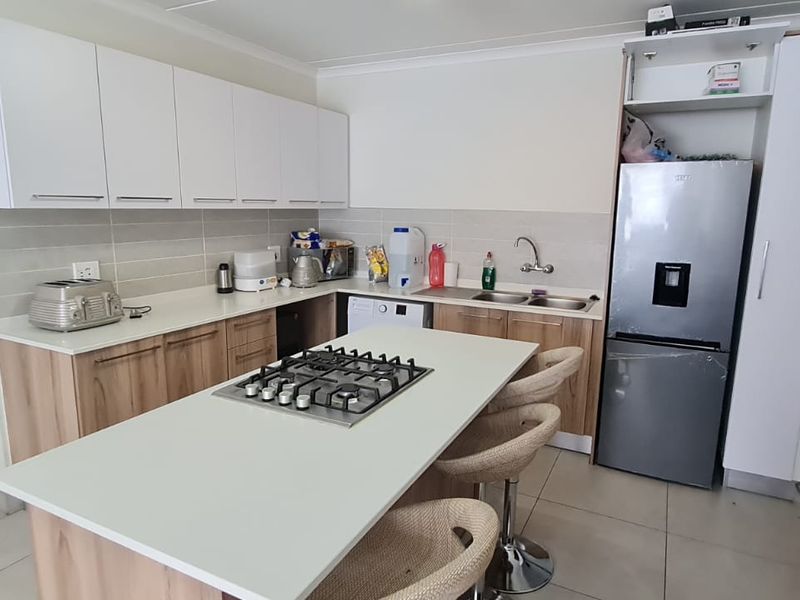 Modern kitchen featuring a central island with a gas hob, ample built-in cabinetry, stone countertops, and tiled flooring.
