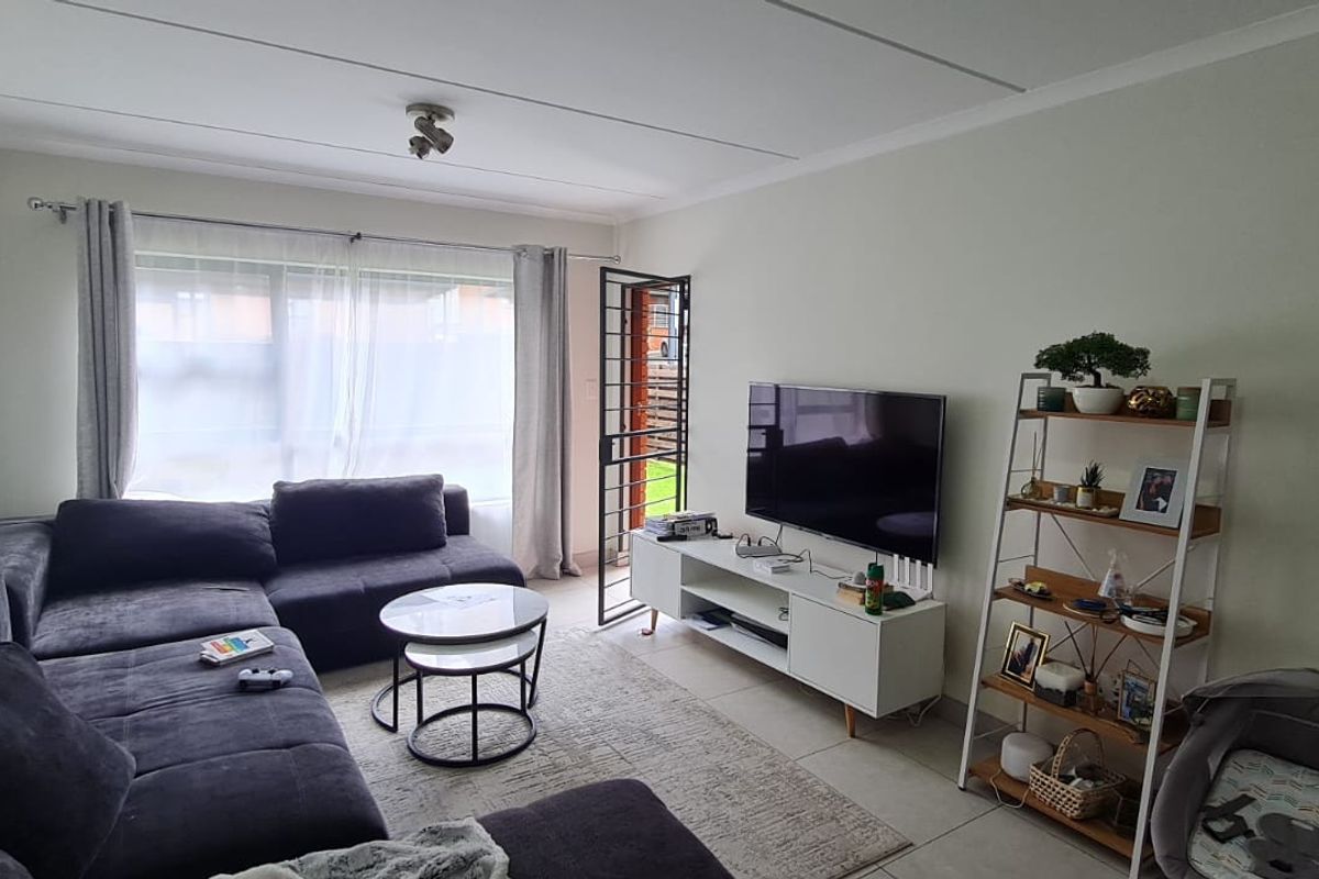 A comfortable living room featuring tiled flooring, a large window for natural light, and a security gate leading to the exterior.