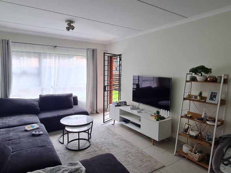 A comfortable living room featuring tiled flooring, a large window for natural light, and a security gate leading to the exterior.