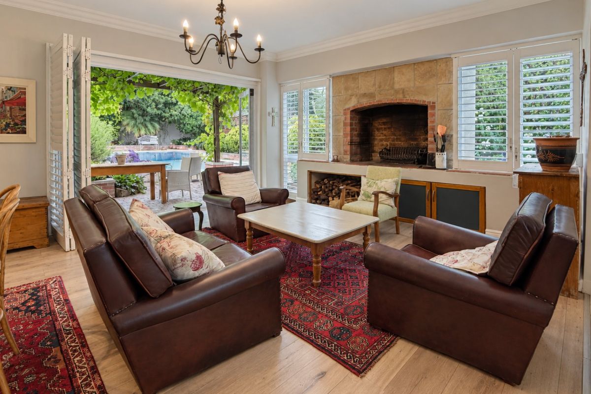 Spacious living room featuring a stone fireplace, timber flooring, and large folding doors that open onto a patio and pool area.