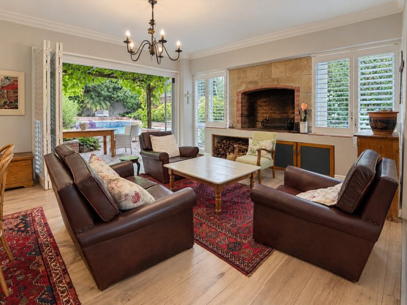 Spacious living room featuring a stone fireplace, timber flooring, and large folding doors that open onto a patio and pool area.